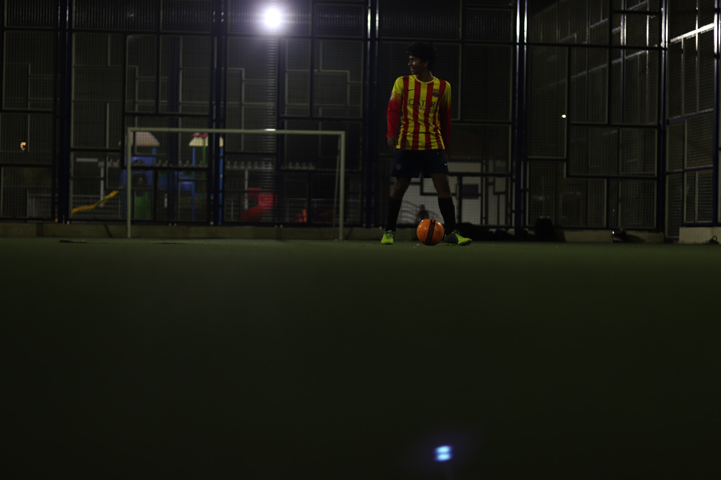 Aditya standing with a football on an indoor pitch at night